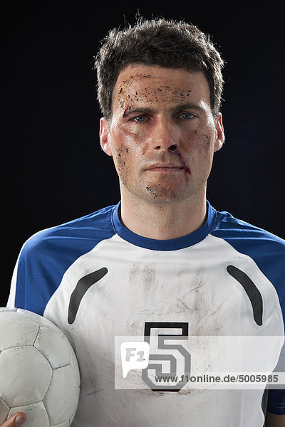 Ein Fußballspieler mit einer blutigen Nase  die einen Fußball hält.