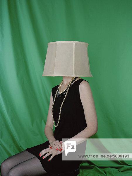 Eine gut gekleidete Frau  die einen Lampenschirm auf dem Kopf trägt.