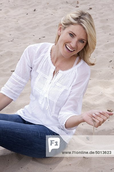 Blonde Frau sitzt im Sand