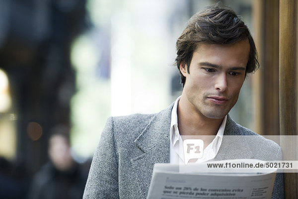 Mann lehnt sich an die Wand und liest Zeitung