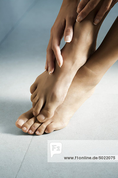 Die Hand der Frau berührt ihre nackten Füße.