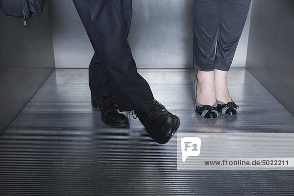 Mann und Frau stehen im Aufzug  Mann bewegt sich mit dem Fuß auf den Fuß der Frau zu.