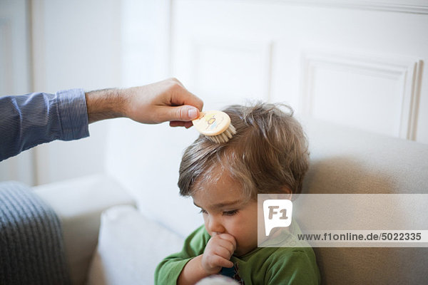 Father brushing toddler son's hair  cropped