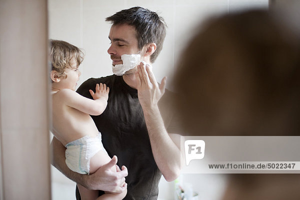 Father showing toddler son how to apply shaving cream