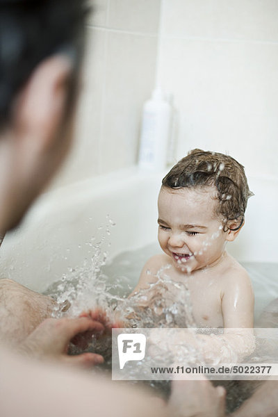 Kleinkind Junge  der mit seinem Vater in der Badewanne spritzt.