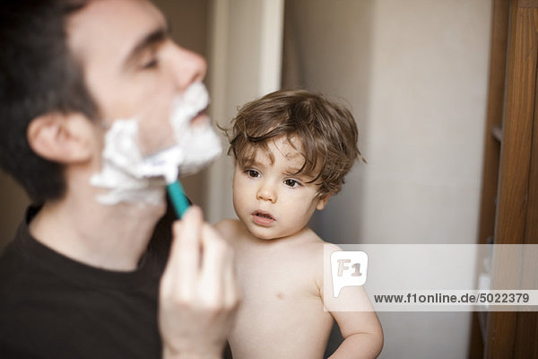 Toddler boy watching his father shave