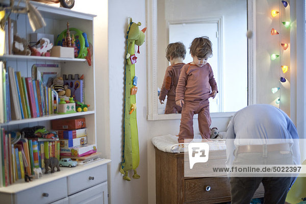 Toddler boy standing on top of changing table in nursery