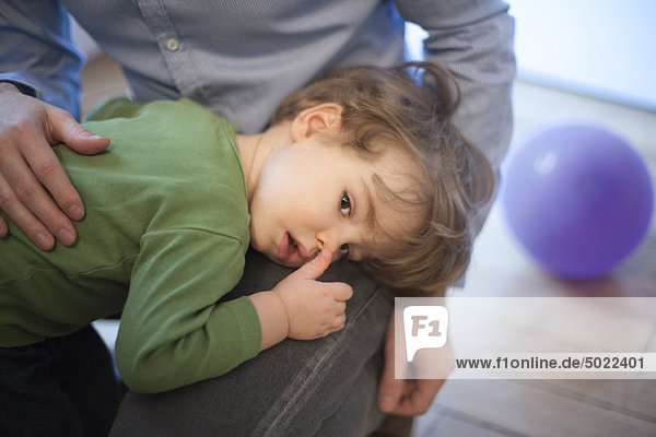 Toddler boy resting head on father's lap