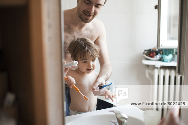 Father and toddler son brushing their teeth together