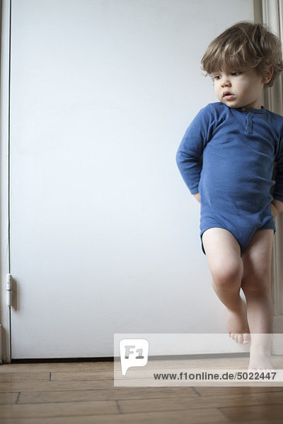 Toddler boy standing on one leg against door  looking away in thought  portrait