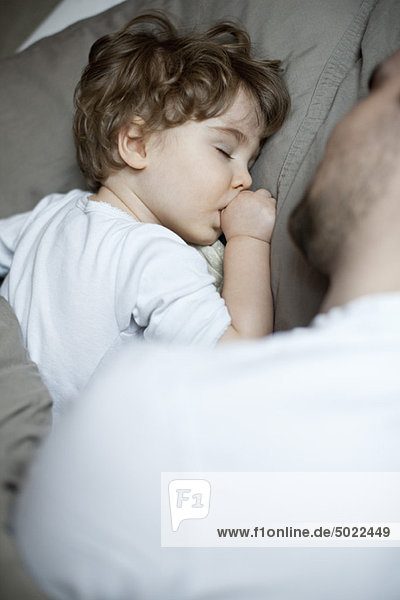 Toddler boy sleeping beside father  cropped