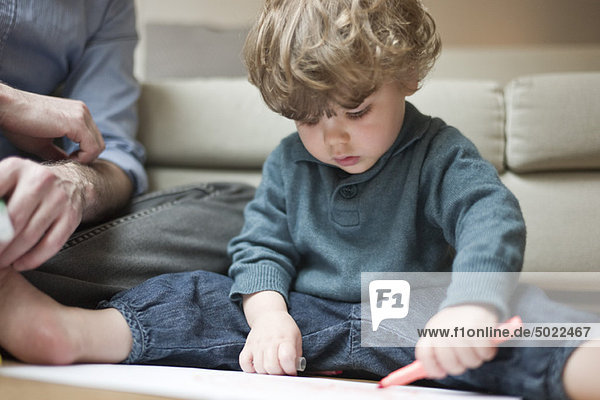 Kleinkind Junge sitzend auf dem Boden mit Vater  Zeichnung auf Papier