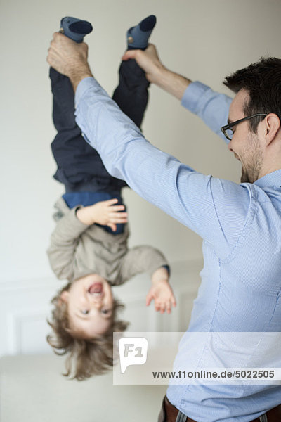 Father holding young son upside down by his ankles