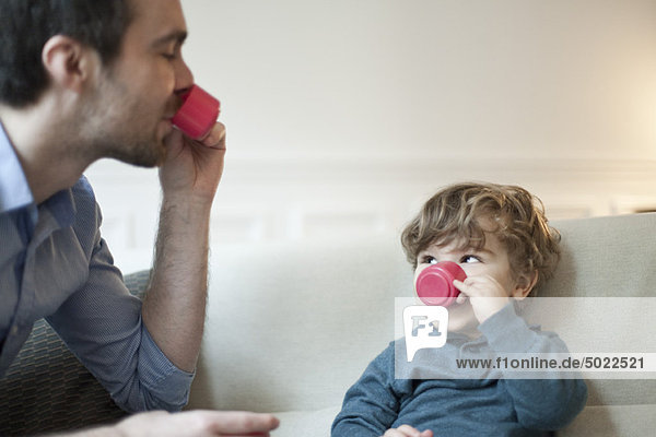 Father and toddler son pretending to drink tea with toy tea cups