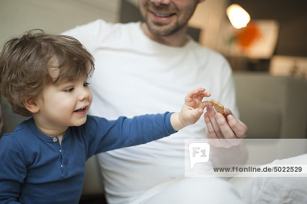 Kleinkind Junge greift nach Keksen in Vaters Hand