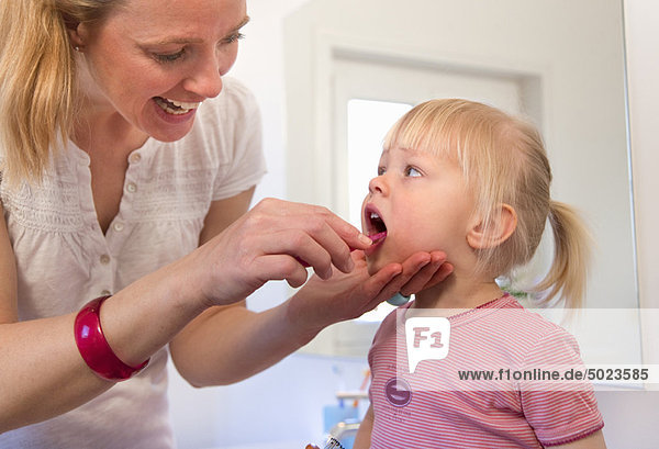 Mother brushing toddler daughter’s teeth