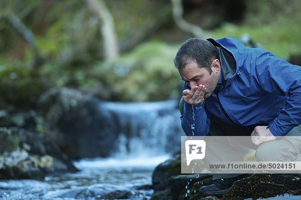 Mann trinkt Wasser aus dem Bach