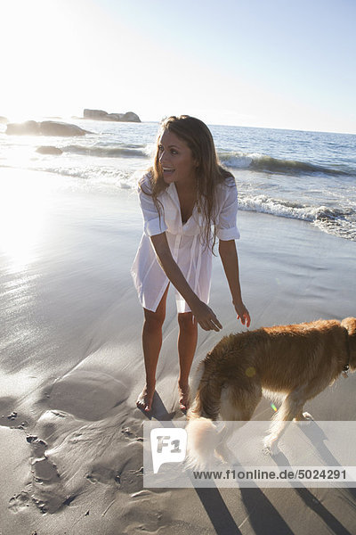 Frau streichelt Hund am Strand
