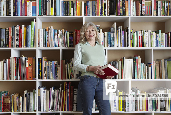 Older woman holding book by bookshelves