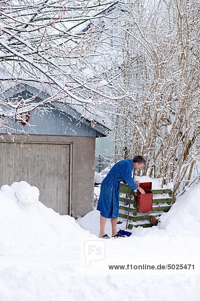 Man in bathrobe checking mail in snowy yard