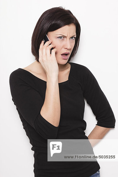 Mittlere erwachsene Frau im Gespräch auf dem Handy vor weißem Hintergrund