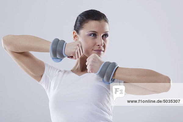 Mid adult woman with wrist weights against white background
