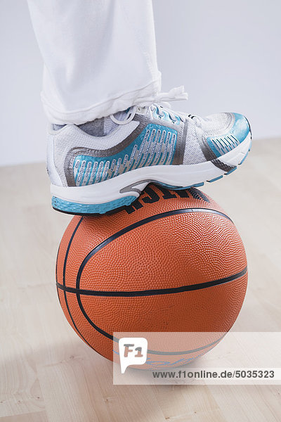 Nahaufnahme des Beines auf Basketball vor weißem Hintergrund