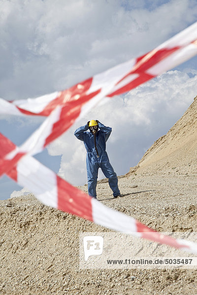 Man in protective wear on sand dune and cordon tape in foreground