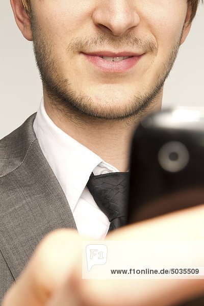 Geschäftsmann hält Handy vor weißem Hintergrund  lächelnd  Nahaufnahme