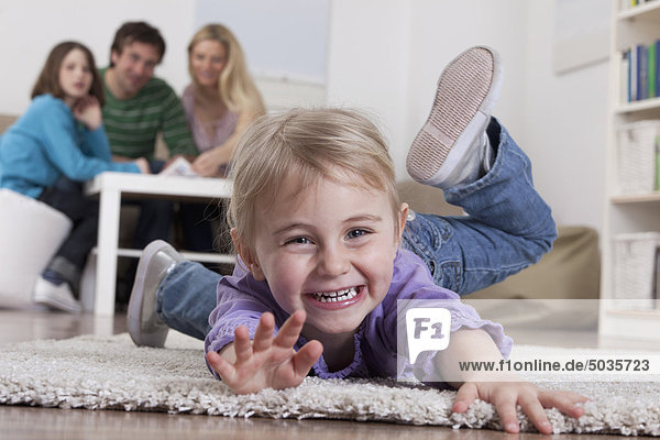 Girl lying on carpet with family sitting in background