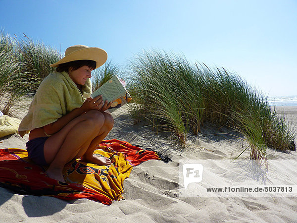 Young woman sitting reading book on sand dune in Cannon Beach  Oregon  USA