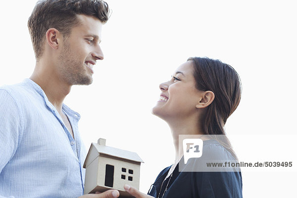 Profile of a young couple holding small model house and looking at each other