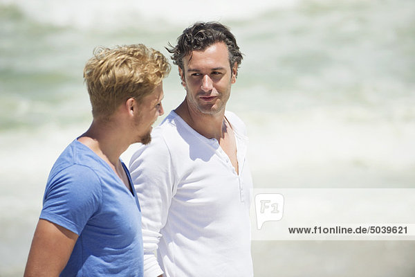 Two men talking while walking on the beach