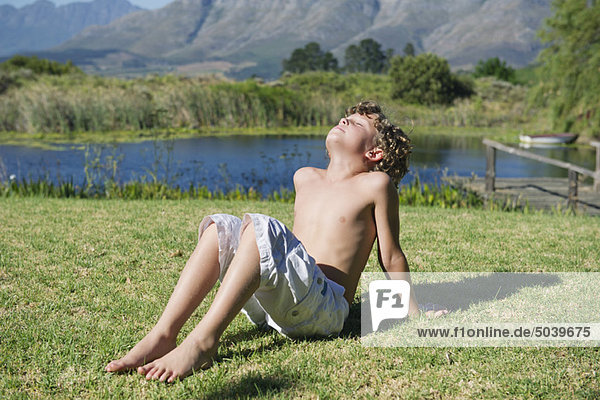 Shirtless little boy sitting with his eyes closed against mountain