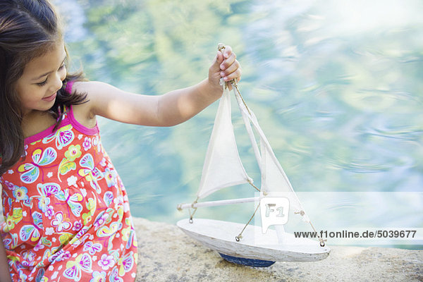 Kleines Mädchen sitzt am Swimmingpool und schaut sich das Modell des Bootes an.