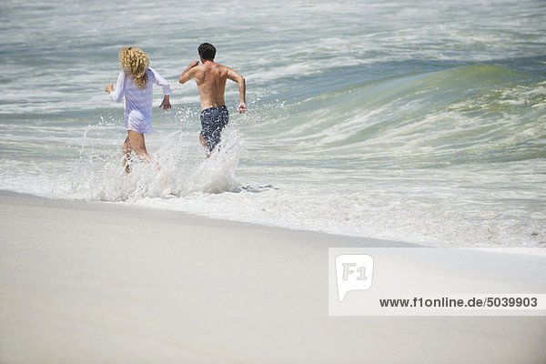 Rear view of a couple running on the beach