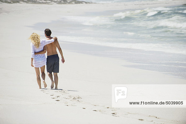 Rückansicht eines Paares  das mit den Armen um den Strand läuft