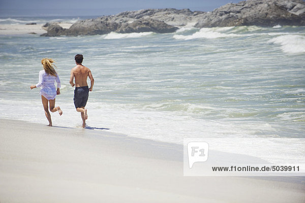 Rear view of a couple running on the beach
