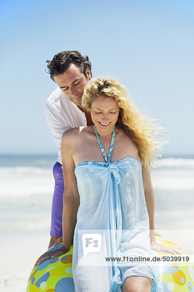 Frau sitzt auf einem Strandball mit einem Mann  der hinter ihr am Strand steht.