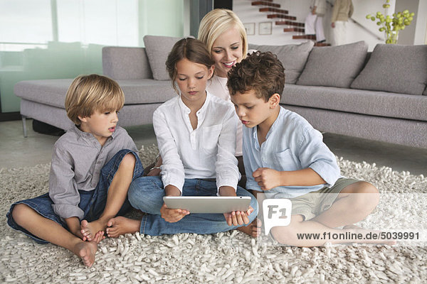 Mädchen  das ein digitales Tablett benutzt  während ihre Mutter und ihre Brüder neben ihr sitzen.
