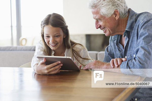Girl using a digital tablet with her grandfather sitting near her