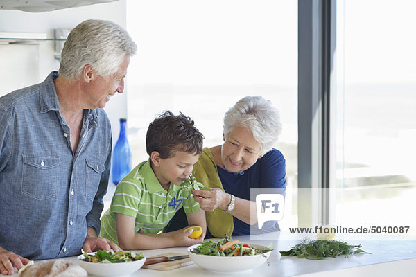 Junge  der Gemüse riecht  während seine Großeltern neben ihm in der Küche stehen.