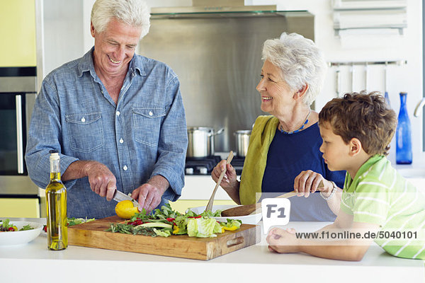 Seniorenpaar beim Zubereiten des Essens mit Enkel auf der Küchenzeile im Haus.