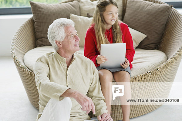 Älterer Mann sitzt mit seiner Enkelin und hält eine digitale Tafel.