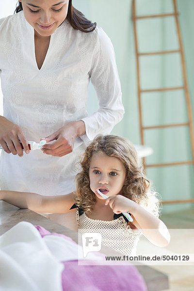 Süßes kleines Mädchen beim Zähneputzen  während die Mutter sie ansieht.