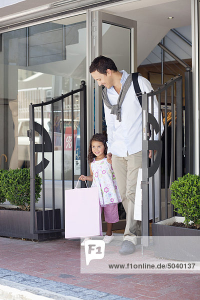 Süßes kleines Mädchen mit ihrem Vater  der aus einem Einkaufszentrum mit Einkaufstaschen kommt.