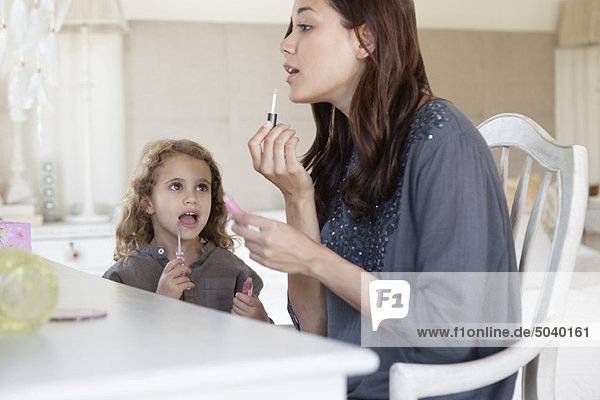 Junge Frau und kleines Mädchen mit Lipgloss am Frisiertisch