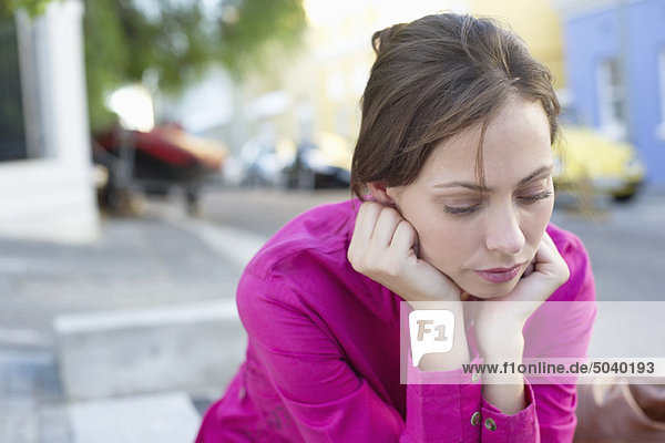 Depressive junge Frau sitzt am Straßenrand