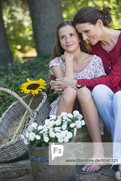 Kleines Mädchen und Mutter sitzend im Freien mit Blumen im Korb