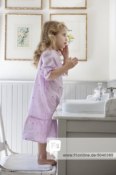 Süßes kleines Mädchen  das auf einem Stuhl vor einem Waschbecken steht.